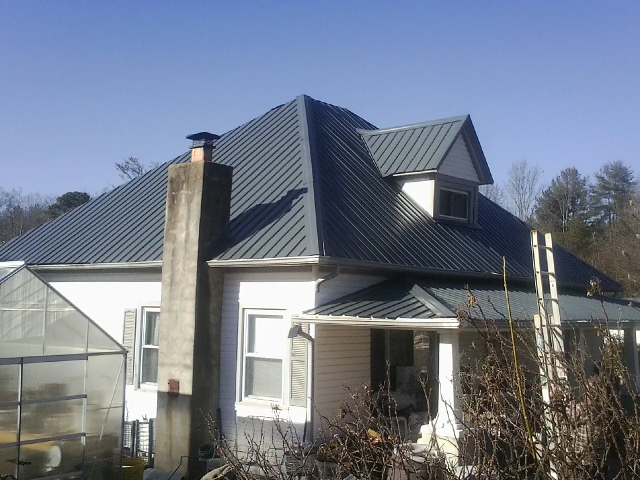 Dark blue standing seam metal roof on a white farmhouse with dormer — Slate & Tile Roof Repair by Roofing Brothers in Matherville