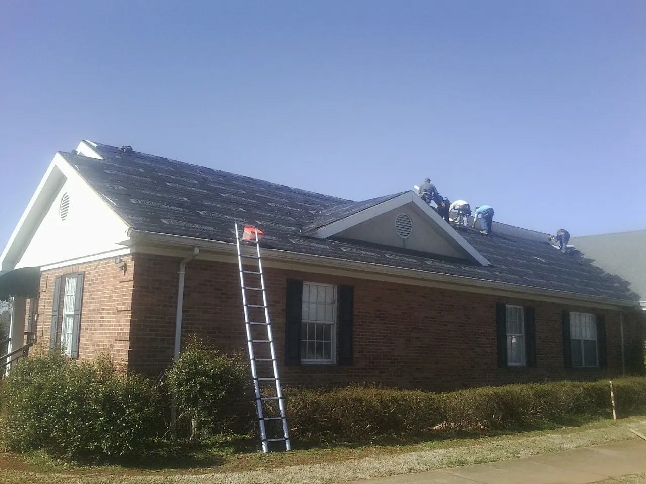Crew tearing shingles off a brick ranch roof with a ladder set — Emergency Roof Repair work by our crew in Matherville