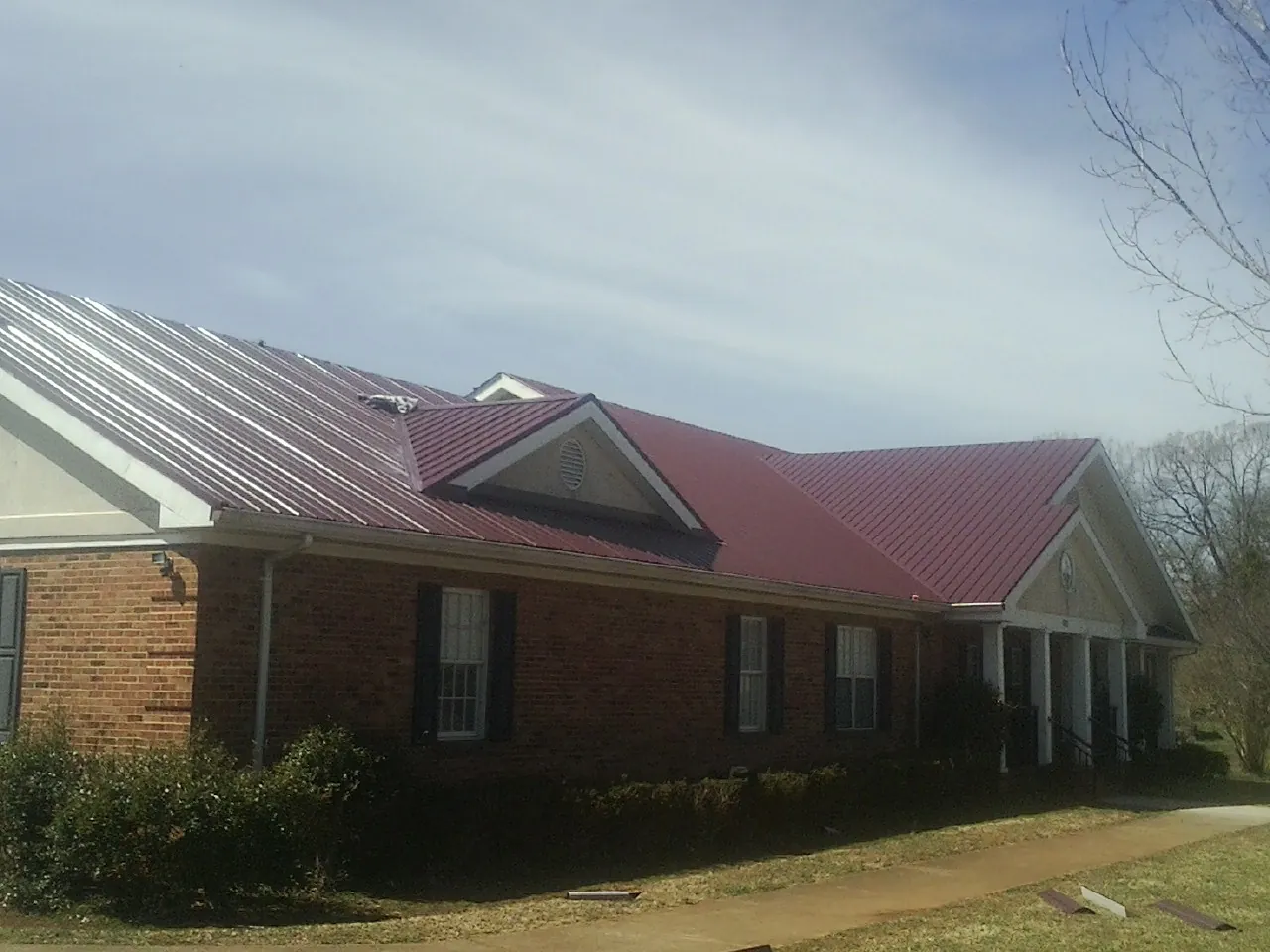 Red metal roof with gabled entries on a long brick building, from a Hail Damage Roof Repair job in Matherville