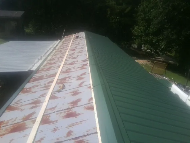 Old rusted panels beside newly installed green metal roofing — Wind Damage Roof Repair by Roofing Brothers in Matherville