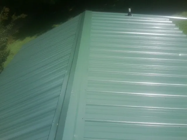 New green metal panels meeting at the ridge of a roof — Flat Roof Repair work by our crew in Matherville
