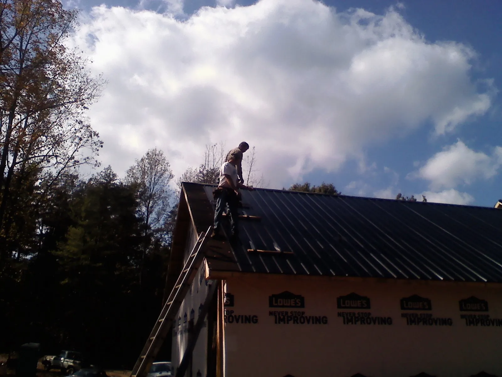 Roofer fastening dark metal panels high against a cloudy sky, from a Roof Inspection job in Matherville