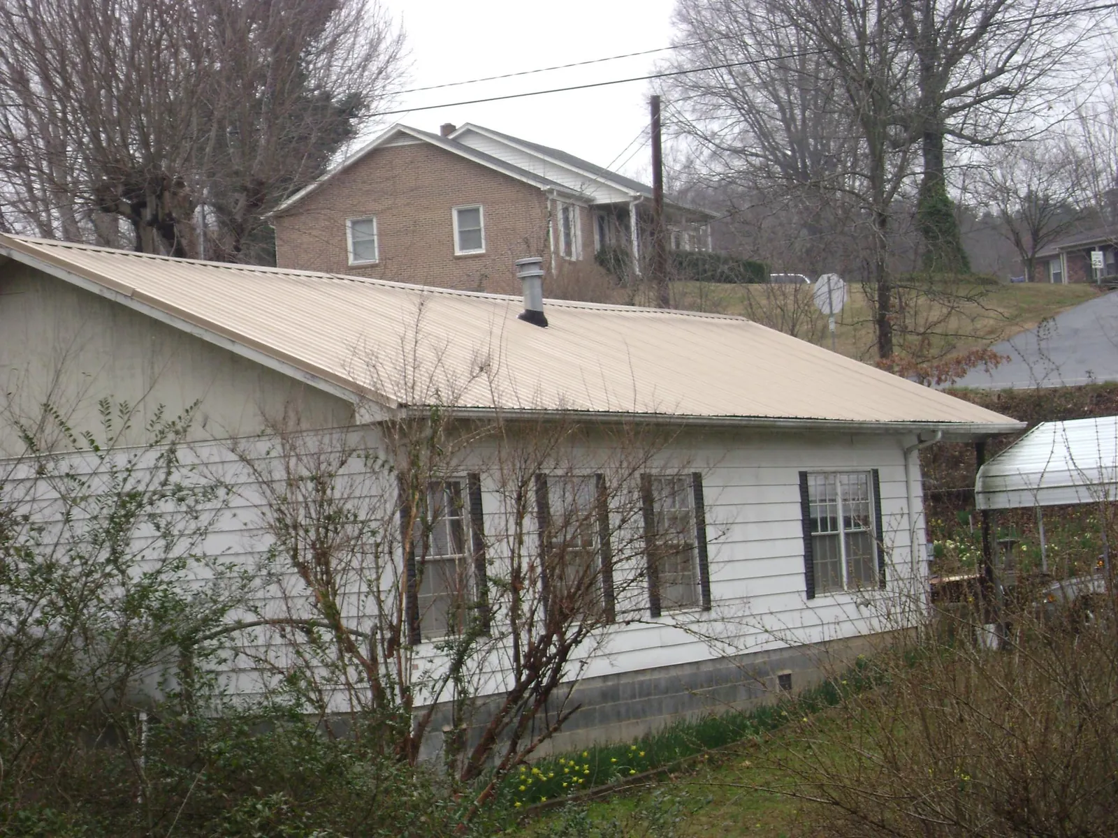 Tan metal roof on a white sided house set into a hillside — Commercial Roofing by Roofing Brothers in Matherville