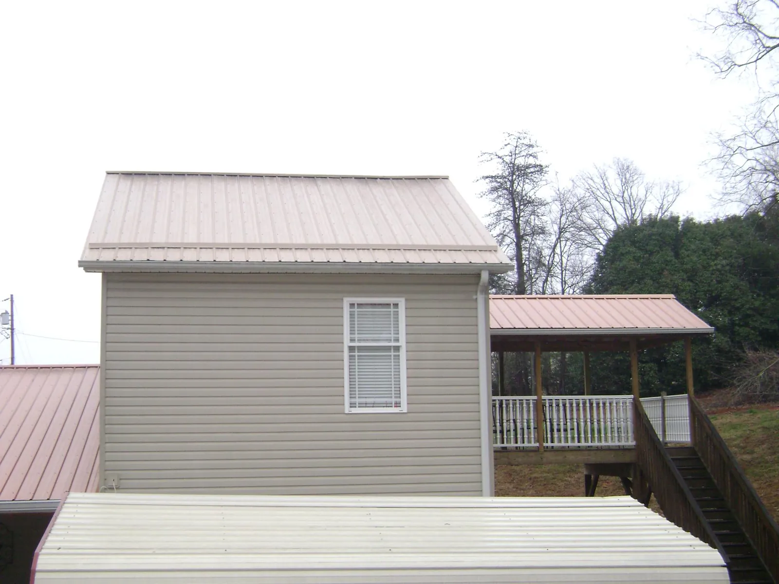 Tan metal roofs on a two story addition and attached porch, from a Roof Replacement job in Matherville